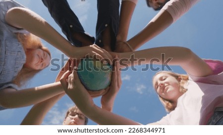 Bottom view of children holding the earth: the future is in their hands. Teen students stand in circle and hold globe outdoors