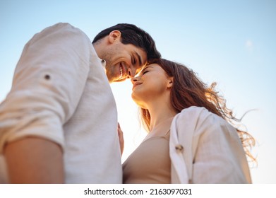 Bottom view close up charming smiling satisfied tender happy young couple two friends family man woman in white clothes boyfriend hug girlfriend enjoy together touch noses on blue light sky background