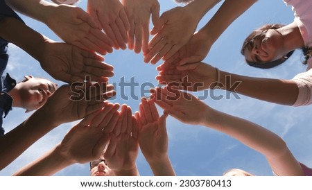 Bottom view of diverse classmates put hands together in circle and raise outdoors. Happy multiethnic teen students join hands in circle outside over blue sky background