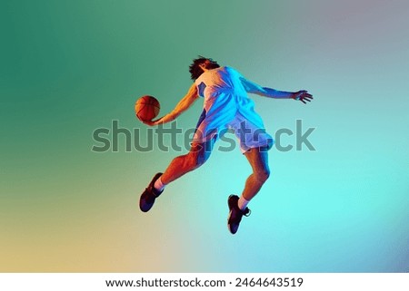 Bottom view dynamic image of young man, basketball player in motion, throwing ball against gradient background in neon light. Concept of sport, competition, active and healthy lifestyle, game