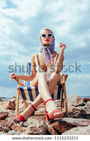 bottom view of elegant attractive girl in retro swimsuit sitting in beach chair  
