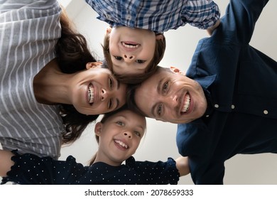 Bottom View Faces Of Happy 35s Couple With Little Adorable Son And Daughter Hugging Standing In Circle Indoors Look At Camera, Having Wide Toothy Smile Advertise Dental Services. Family Bond Concept