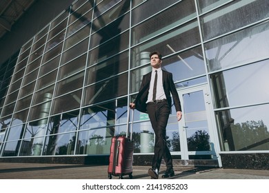 Bottom View Full Size Young Traveler Businessman Man In Black Dinner Suit Walk Go Stand Outside At International Airport Terminal With Suitcase Valise Looking Aside. Air Flight Business Trip Concept.