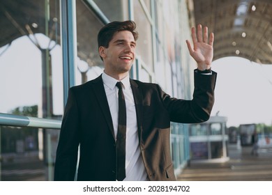 Bottom View Happy Fun Young Traveler Brunet Businessman Man 20s Wear Black Classic Tie Suit Standing Outside At International Airport Terminal Look Aside Waving Hand Air Flight Business Trip Concept