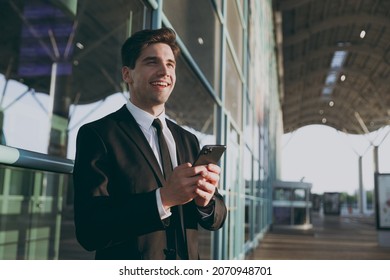 Bottom view happy young traveler businessman man in black suit stand outside at international airport terminal use mobile cell phone book taxi order hotel look aside Air flight business trip concept - Powered by Shutterstock