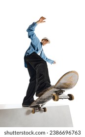 Bottom view image of teen boy in casual clothes in motion, training, doing stunts on skateboard isolated over white background. Concept of professional sport, competition, training, action.