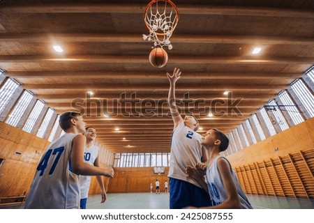 Bottom view of a junior basketball players in action shooting at the hoop during their training on basketball court. Young basketball kids at the hoop shooting a ball. Teamwork at basketball training.