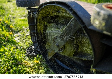 Bottom view of a lawn mower deck with a metal cutting blade covered in wet green grass clippings after backyard mowing.