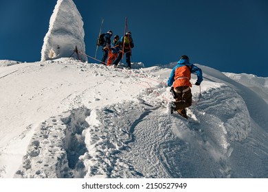 bottom view of man in ski suit holding a rope and climbing a mountain slope covered with powdery snow