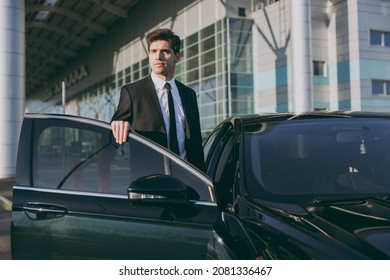 Bottom view minded young traveler brunet businessman man 20s wearing black classic tie suit stand outside at international airport terminal gets into car taxi. People air flight business trip concept.