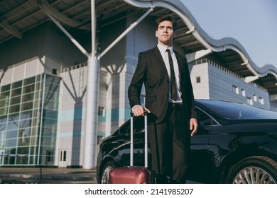 Bottom view minded young traveler businessman young man in black dinner suit going walk outside at international airport terminal with suitcase near car booking taxi Air flight business trip concept.