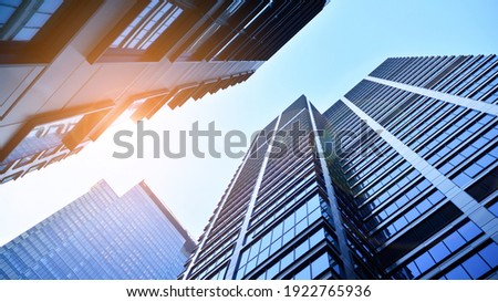 Bottom view of modern skyscrapers in business district against blue sky. Looking up at business buildings in downtown. Rising sun on the horizon.