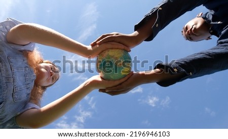 Bottom view of multiethnic teen students hold globe of the earth standing outdoors over blue sky background. Environment and ecology concept