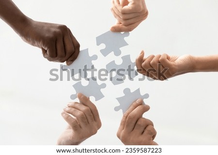 Bottom view of multiracial colleagues join puzzle pieces search for best business solution in group, diverse coworkers put together jigsaw parts, engaged in teambuilding activity, teamwork concept
