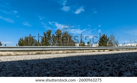 Bottom view of a paved road. In the background the guard rail and the blue sky. 