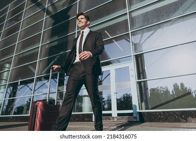 Bottom View Pensive Young Traveler Businessman Man 20s In Black Dinner Suit Walk Go Stand Outside At International Airport Terminal With Suitcase Valise Look Aside. Air Flight Business Trip Concept.