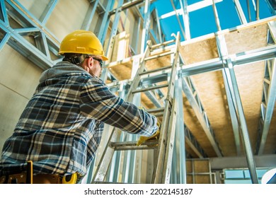 Bottom View Photo Of Professional Construction Worker Wearing Yellow Safety Helmet Climbing The Extension Ladder To Reach The Next Floor At New Commercial Warehouse Building Site.