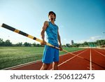 Bottom view portrait of focused and determined pole vaulter, athlete in blue uniform standing with pole at open air stadium, showing readiness to train. Concept of sport, tournament, active lifestyle