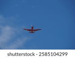 Bottom view of a red US Navy training aircraft in flight against a blue sky