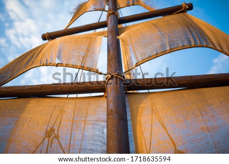 Bottom view of a ship mast with beige sails swings against a blue sky with sunny sunny summer warm day clouds. Marine and adventure concept