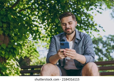 Bottom view smiling happy fun nyoung man in blue shirt sit on bench use mobile cell phone chat online rest relax in spring green city sunshine park outdoors on nature Urban lifestyle leisure concept. - Powered by Shutterstock