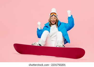 Bottom view snowboarder woman wear blue suit goggles mask hat ski padded jacket sit do winner gesture isolated on plain pastel pink background. Winter extreme sport hobby weekend trip relax concept