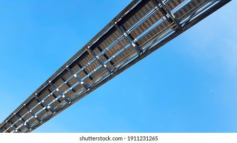 Bottom view of stainless steel electrical or communication cable tray with clear blue sky background. Iron bridge cross to air or heaven and industrial and installed system concept.