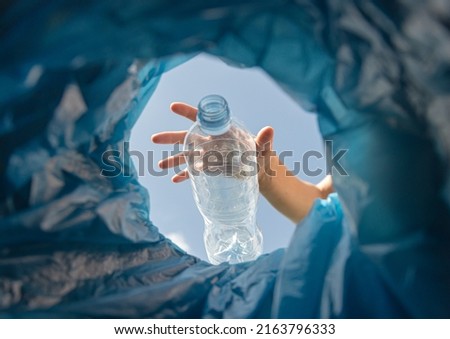 bottom view of trash bins and assorted garbage. woman hand throws a plastic bottle into a garbage can