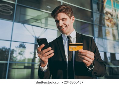 Bottom view traveler businessman man wear black suit stand outside at international airport terminal use mobile cell phone hold credit bank card doing online payment Air flight business trip concept. - Powered by Shutterstock