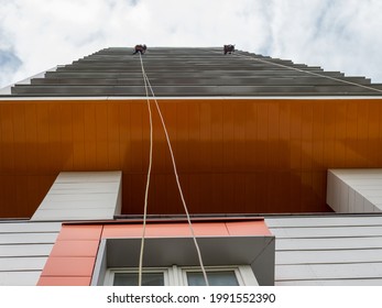 Bottom view of two window washers hanging from safety ropes.