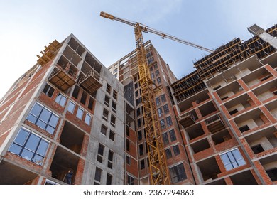 Bottom view of an unfinished multi-story residential building under construction with a working construction crane against a clear blue sky - Powered by Shutterstock