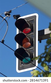 Bottom view of a vertical traffic light with a red signal illuminated against a clear blue sky.
