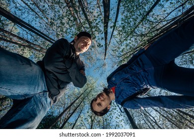 Bottom View Of Woman And Man In The Forest On The Background Of Tops Of Tall Trees And Blue Sky. Young Couple In Casual Wear Walks In The Woods. Wide Angle Shot Of Hikers In Nature. Summer Adventures