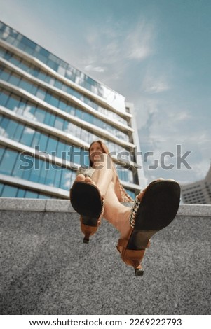 Bottom view of a woman sitting on a marble fence illuminated by a sun-soaked sky. Low angle view at soles of female sandals