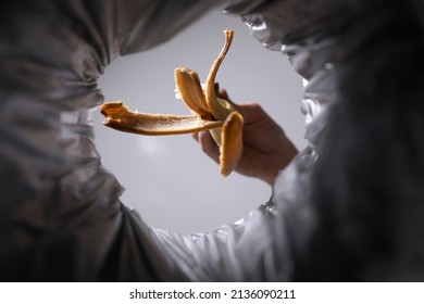 Bottom View Of Woman Throwing Banana Peel Into Trash Bin On Grey Background, Closeup