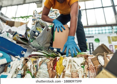 Bottom view of young african american man sorting waste paper while standing on large pile of rubbish, cropped. Garbage sorting and recycling concept