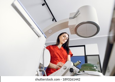 Bottom view of young attractive Caucasian female doctor in red uniform, working with modern lithotripter equipment for treatment of kidney stones. Non-invasive extracorporeal shock wave lithotripsy