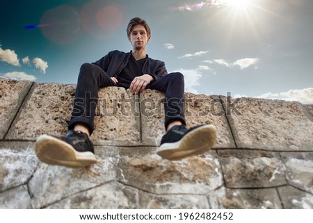 Bottom view of young Caucasian male sitting on stones of pier.