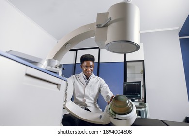 Bottom view of young confident African doctor in white uniform, working with modern lithotripter equipment for treatment of kidney stones. Non-invasive extracorporeal shock wave lithotripsy