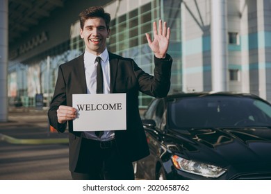 Bottom View Young Friendly Traveler Businessman Man Wear Black Suit Stand Outside At International Airport Terminal Hold Card Sign With Welcome Title Text Waving Hand Air Flight Business Trip Concept.