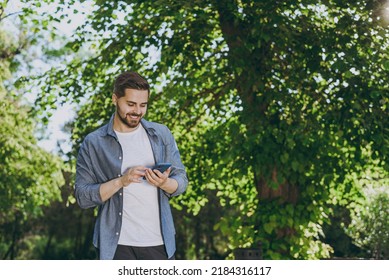 Bottom view young smiling man in blue casual shirt walk use mobile cell phone rest relax in spring sunshine forest green city park go down alley outdoors on nature. Urban lifestyle leisure concept. - Shutterstock ID 2184316117