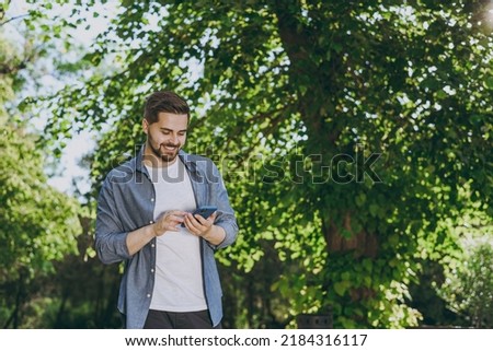 Bottom view young smiling man in blue casual shirt walk use mobile cell phone rest relax in spring sunshine forest green city park go down alley outdoors on nature. Urban lifestyle leisure concept.