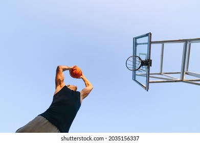 Bottom View Young Sporty Sportsman Man In Sports Clothes Train Shooting Free Throw Scoring Basket Play With Ball At Basketball Game Playground Court On Sky Background Outdoor Courtyard Sport Concept.