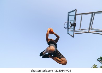 Bottom View Young Strong Sportsman Man In Sports Clothes Train Shooting Free Throw Scoring Basket Play With Ball At Basketball Game Playground Court, Sky Background Outdoor Courtyard Sports Concept.