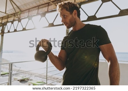 Bottom view young strong sporty athletic toned fit sportsman man wearing sports clothes warm up training work out lifts weight kettlebell at outdoor gym sea beach outdoor seaside in summer day morning