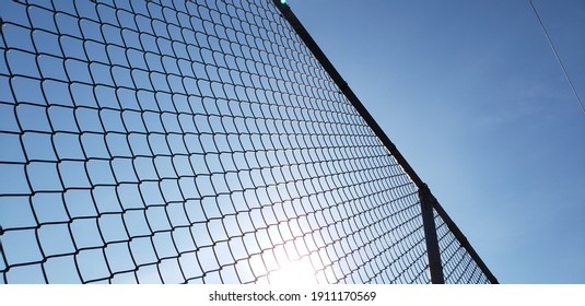 A bottoms up view with the perspective of looking up through a chain link metal fence. The sun is glaring through the mesh and an electrical line is in the distance. Angled and textured background pic