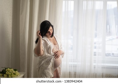 Boudoir Maternity Photoshoot: Pregnant Brunette Caucasian Woman Wearing Beautiful Lingerie And A Beige Robe