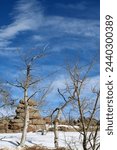 Boulder fields of Vedauwoo in Wyoming. Snow covered boulders in Medicine Bow -Routt National Park with bare trees. Vedauwoo boulders in morning sun with dark blue sky and wispy clouds in winter.