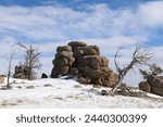 Boulder fields of Vedauwoo in Wyoming. Snow covered boulders in Medicine Bow -Routt National Park with bare trees. Vedauwoo boulders in morning sun with dark blue sky and wispy clouds in winter.