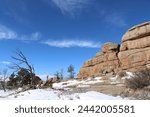 Boulder fields of Vedauwoo in Wyoming. Snow covered boulders in Medicine Bow -Routt National Park with bare trees. Vedauwoo boulders in morning sun with dark blue sky and wispy clouds in winter.